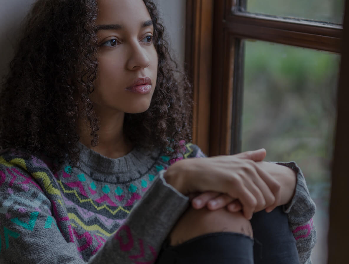 young woman sitting inside looking out window